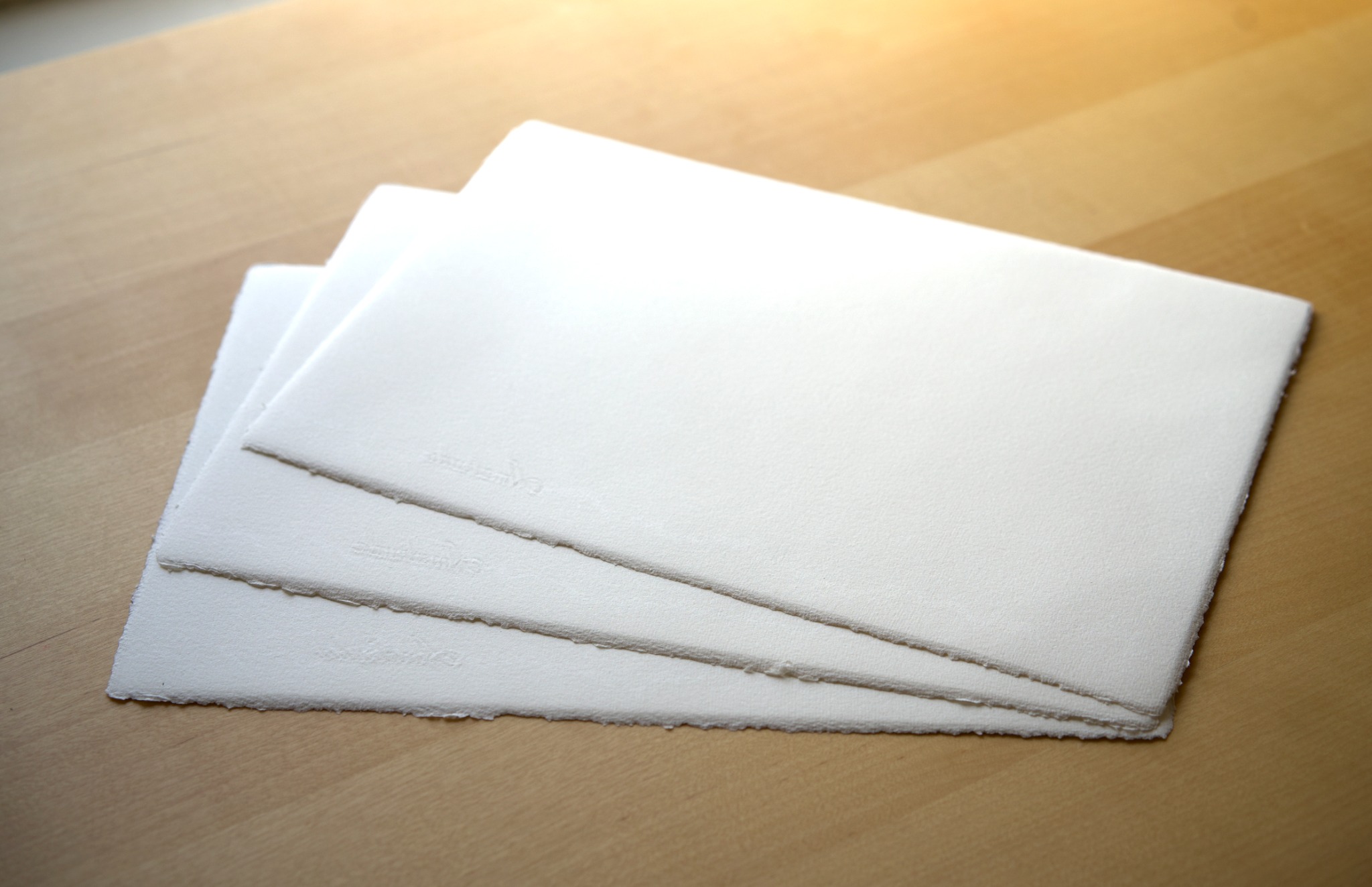 Three sheets of handmade Amalfi watercolour paper with deckle edges on a wooden table